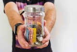 A man holds out a jar of Australian cash.