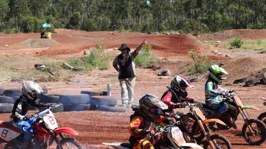 Man standing with hand up directing motocross racers