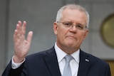 Scott Morrison holds one hand in the air while standing in the PM's courtyard at Parliament House