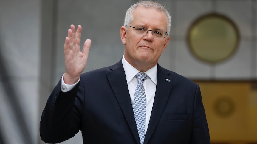 Morrison holds a hand in the air while speaking to media.