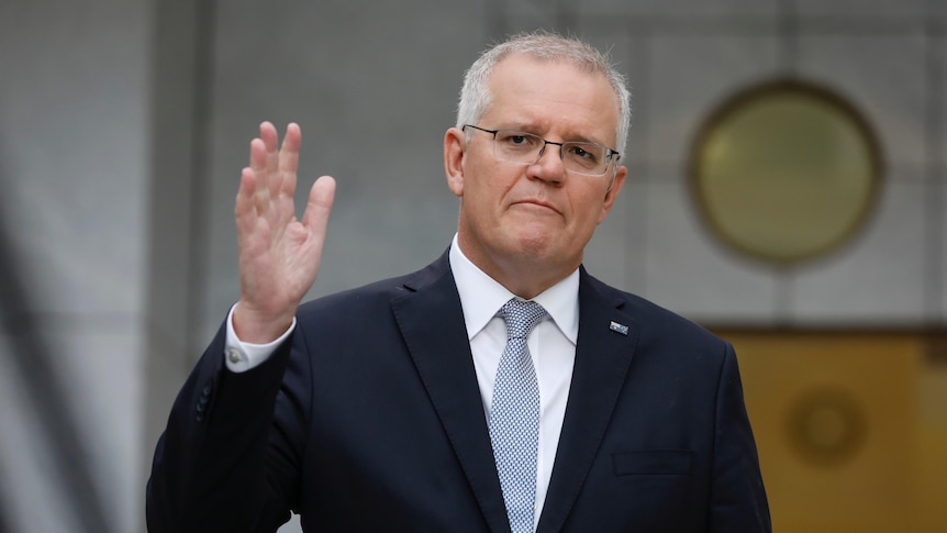 Scott Morrison holds one hand in the air while standing in the PM's courtyard at Parliament House