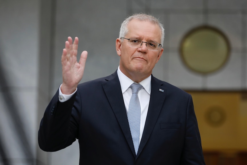 Scott Morrison holds one hand in the air while standing in the PM's courtyard at Parliament House