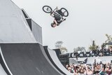 A woman doing a flip on a BMX bicycle as a crowd cheers