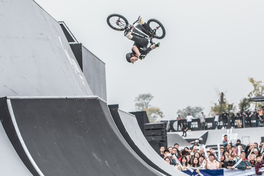 A woman doing a flip on a BMX bicycle as a crowd cheers