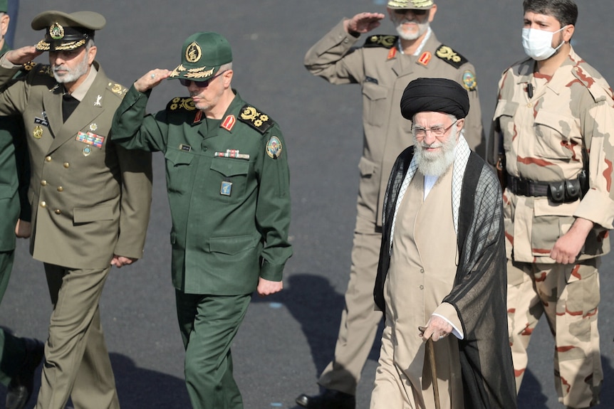 L'ayatollah Ali Khamenei portant des robes utilise une canne tout en marchant avec des hommes vêtus d'uniformes militaires.