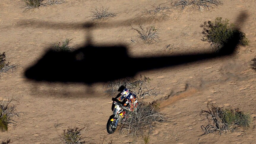 Photographer in helicopter takes photo of helicopter shadow next to Toby Price as he races through arid landscape.