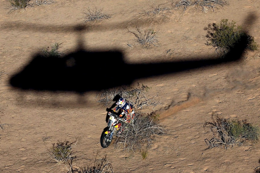 Photographer in helicopter takes photo of helicopter shadow next to Toby Price as he races through arid landscape.