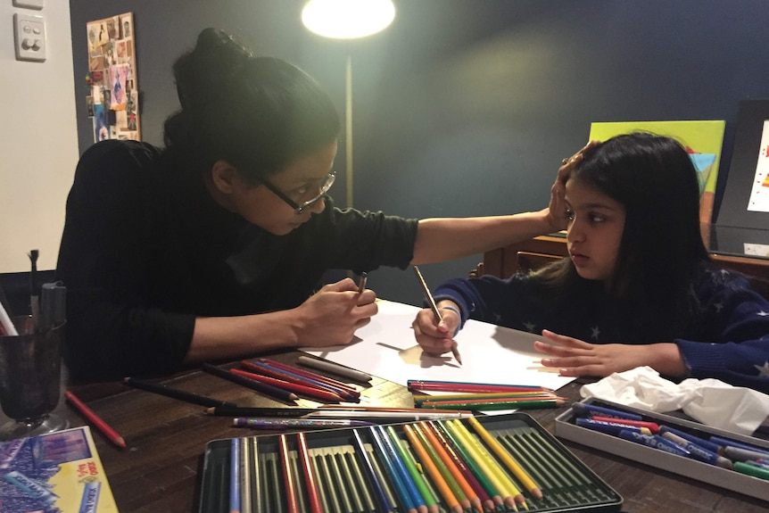 A woman and a young girl sitting at a table with coloured pencils.