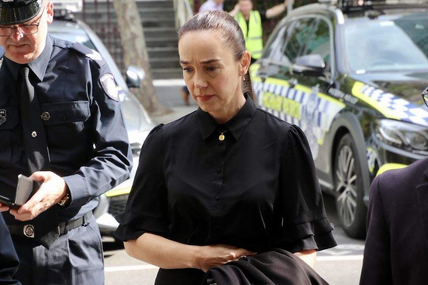 A photo of a woman dressed in black surrounded by police officers.