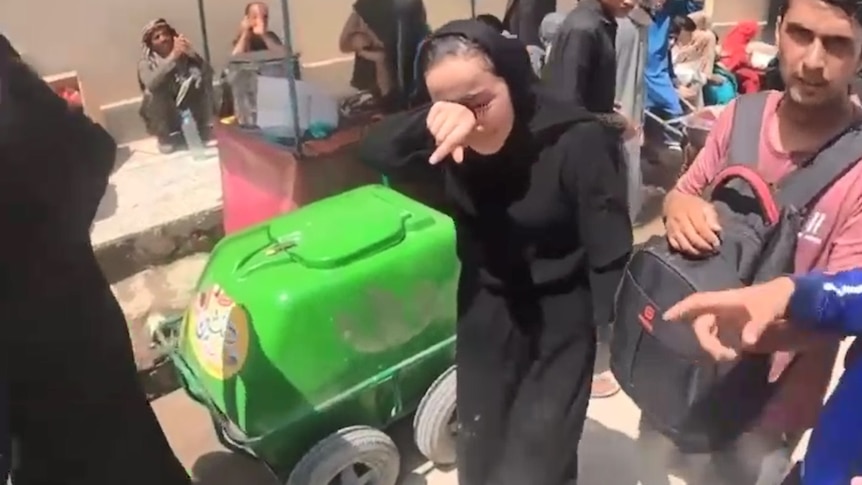Zakia Khudadadi cries and wipes her face wearing black with people around her