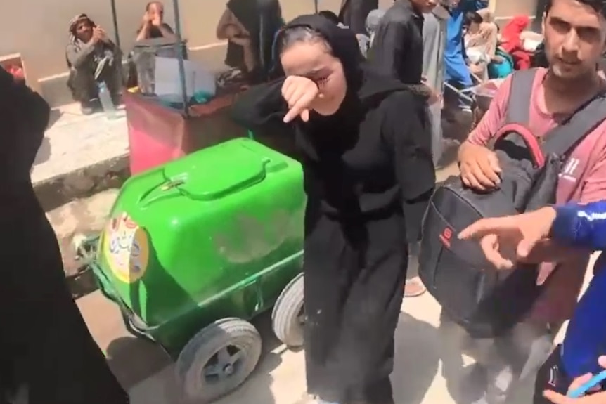 Zakia Khudadadi cries and wipes her face wearing black with people around her