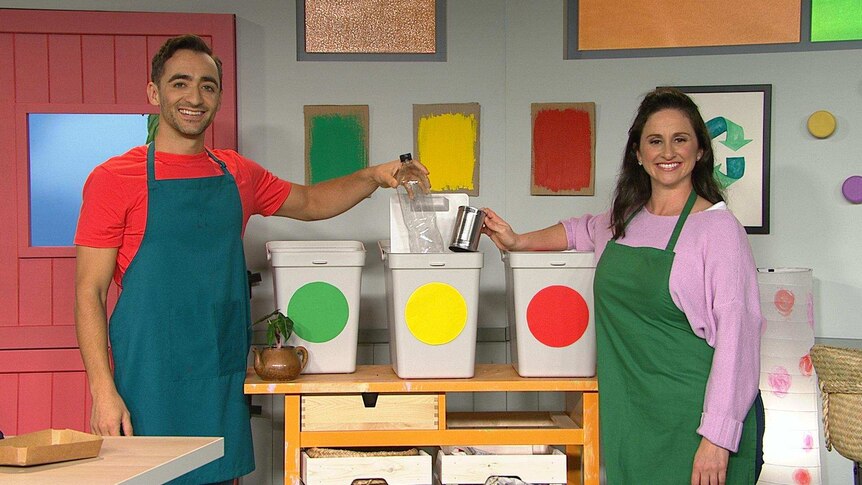 Matt and Emma both wearing an apron putting items into a small bin.