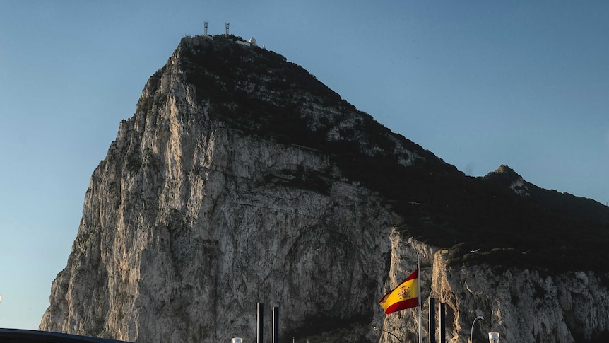 The rock of Gibraltar looms large over a Spanish border point marked by a Spanish flag in the foreground.