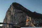 The rock of Gibraltar looms large over a Spanish border point marked by a Spanish flag in the foreground.