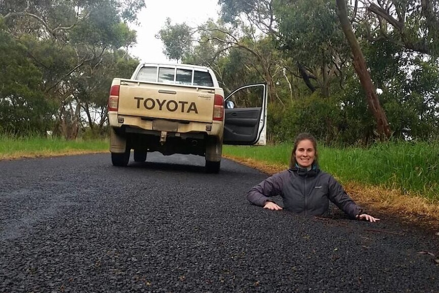 Woman stands in sinkhole on road