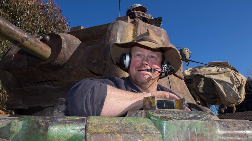 A man wearing a floppy felt hat over earphones and a headset in the cabin of a tank