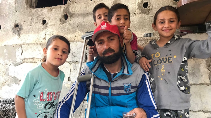 Amed Abead sits with his crutches surrounded by his children