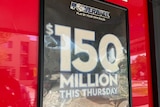 A dark blue sign advertising a $150 million lottery prize is mounted on a shiny red wall.