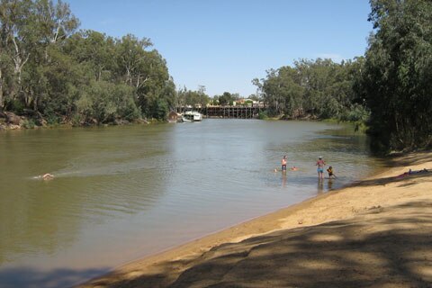 Tree-lined wide river with sandy beach where people are swimming and sunning themselves