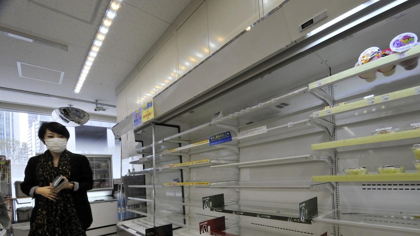 Japanese woman walks past empty supermarket shelves