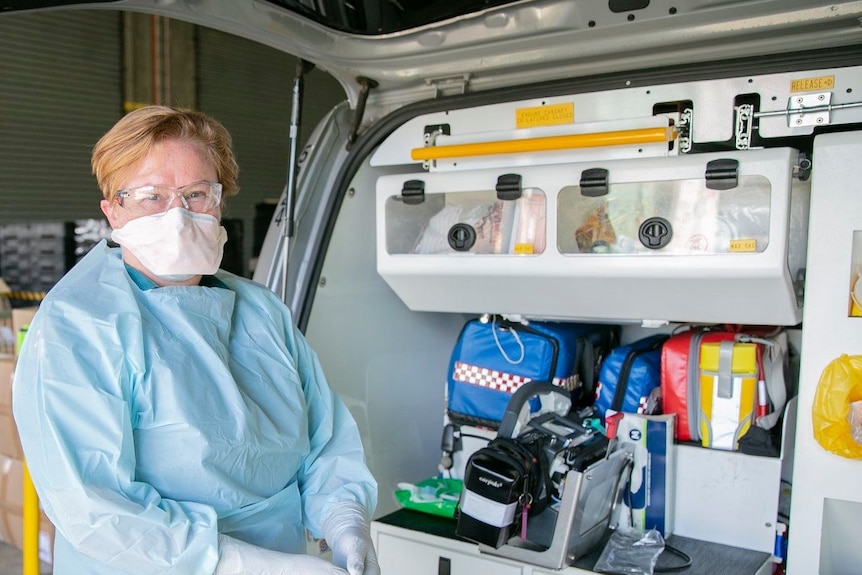 Paramedic with a face masks stands next to the back of her ambulance.