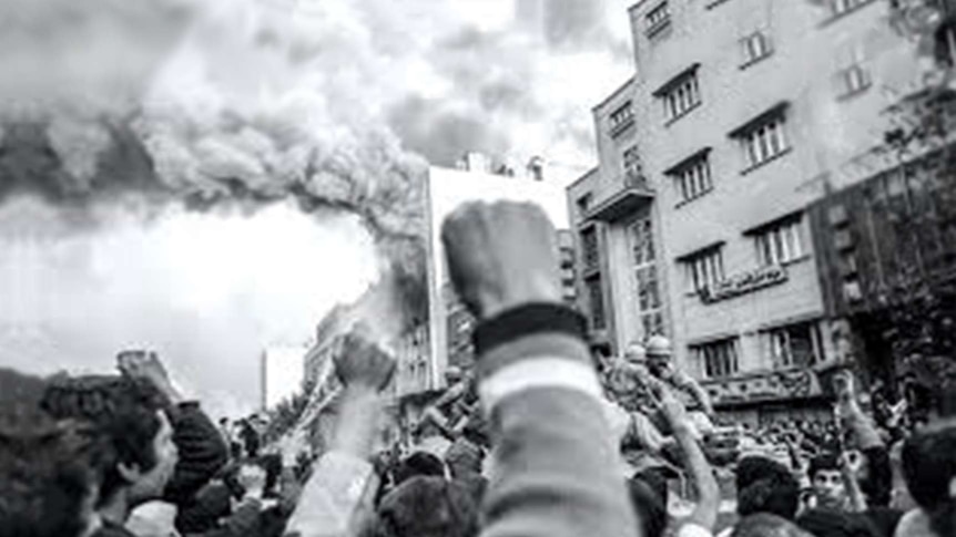 A hand is raised in a fist amid a crowd below a burning building