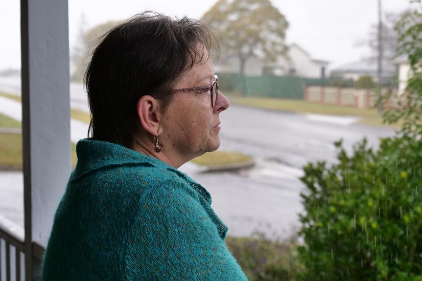 An older woman looks out from her balcony on a rainy day.