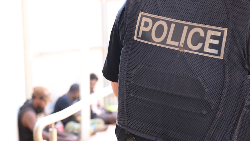 A policeman stands at the entrance of Bush Court in Wadeye, where a queue of people is forming