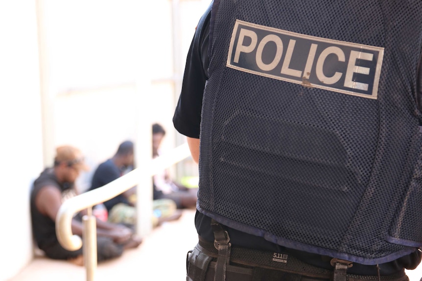 A policeman stands at the entrance of Bush Court in Wadeye, where a queue of people is forming