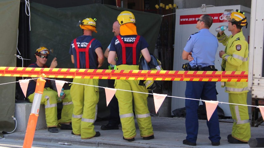 A police officer and Fire and Emergency Services workers stand talking behind a cordon.