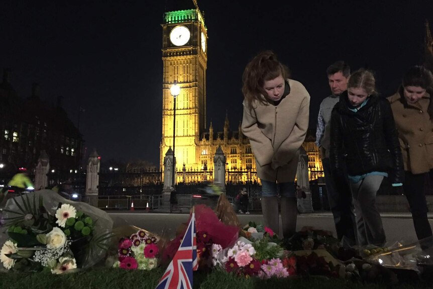 Passers-by look at floral tributes on Westminster bridge with Big Ben lit up in the background