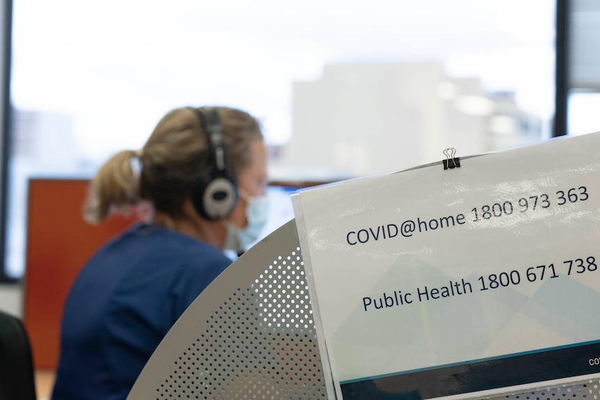 A woman wears a headset behind a sign reading COVID@home