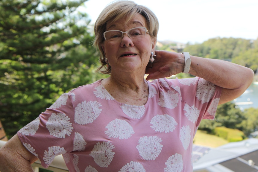 An older woman on a balcony strikes a pose with her hand behind her head.