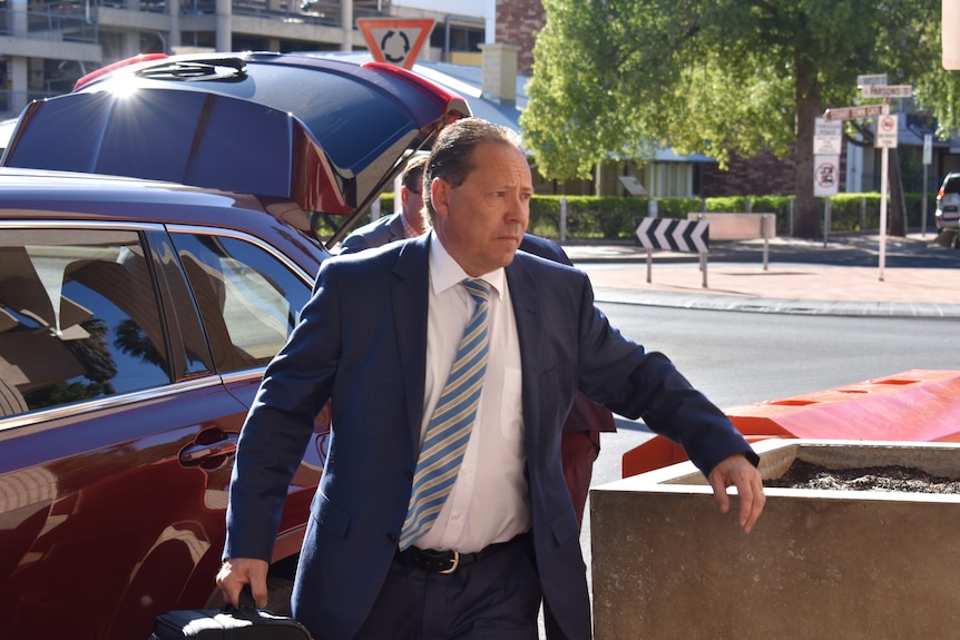 Defence lawyer David Edwardson QC walks out of a car wearing a suit and carrying a briefcase.