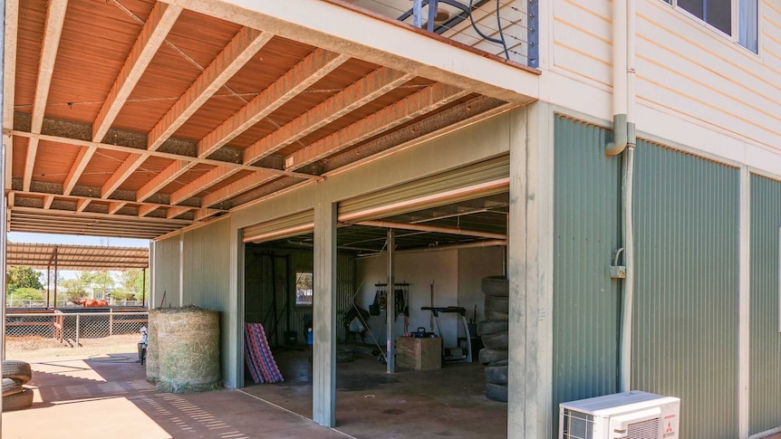 A photo of the bottom story of a house in the outback. You can see gym equipment, hay, and a horse in the background.