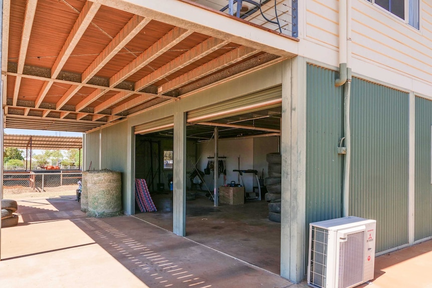 A photo of the bottom story of a house in the outback. You can see gym equipment, hay, and a horse in the background.