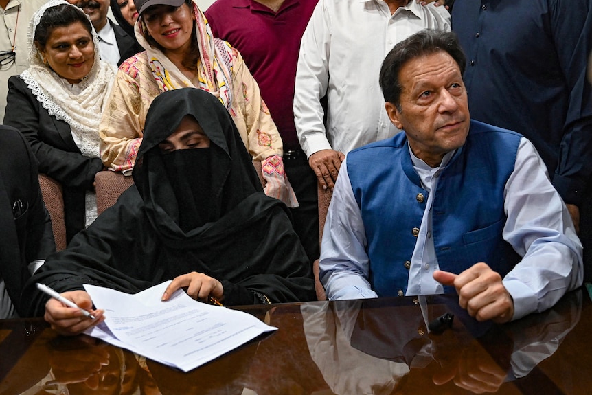 A woman in a black niqab and Imran Khan sitting at a table signing papers. 
