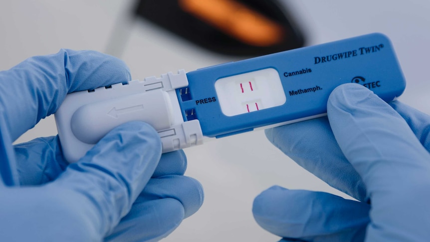 A drug test is held by a pair of gloved hands.