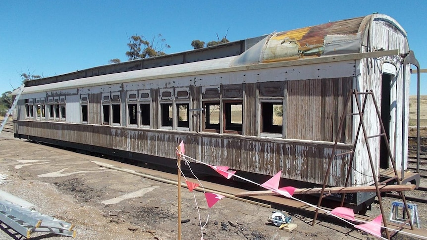 A run down carriage with its white paint peeling sits on some old rusty train tracks.