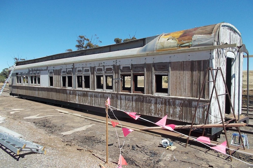 A run down carriage with its white paint peeling sits on some old rusty train tracks.