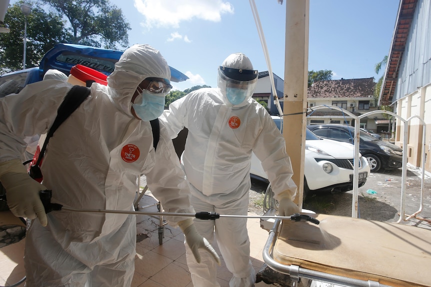 Health workers in protective suits spray disinfectant after carrying the body of a COVID-19 victim