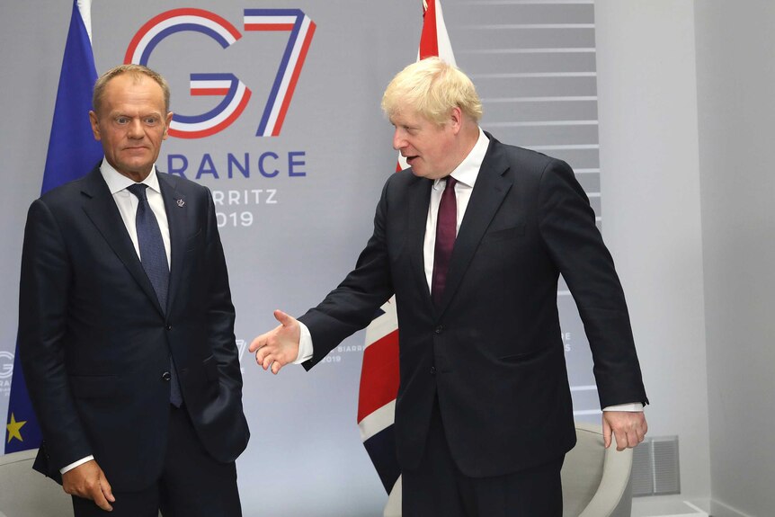 Boris Johnson holds out his arm to shake hands while Donald Tusk looks away.