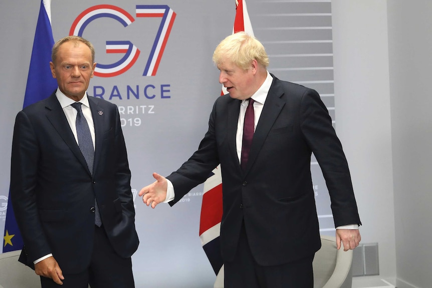 Boris Johnson holds out his arm to shake hands while Donald Tusk looks away.