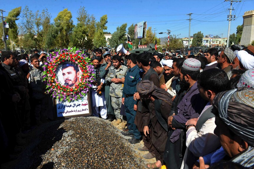 A crowd of people in uniform and traditional afghan outfits stand at the gravesite of General Abdul Razeq