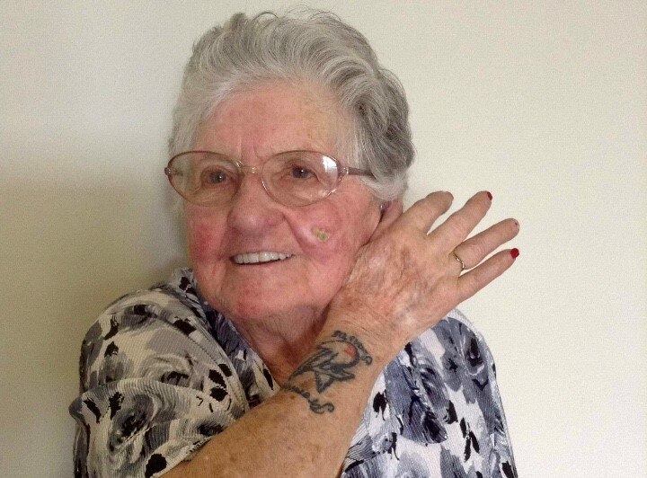 An elderly lady smiles for the camera and shows her Sydney Swans premiership tattoo on her right forearm
