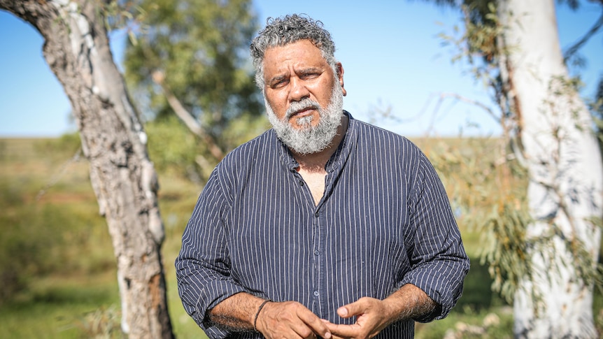 An Aboriginal man stands outside in a dark shirt