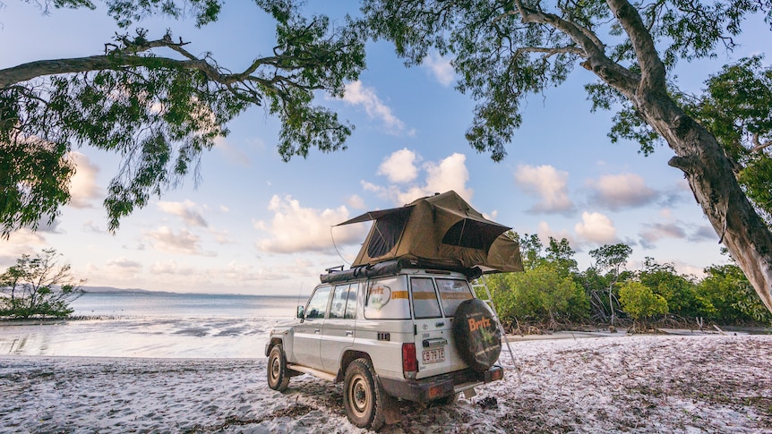 A white troop carrier parked on a beach with white sand facing the water 