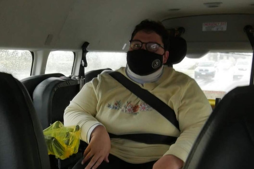 A woman wearing a mask sits in the back of a wheelchair taxi.