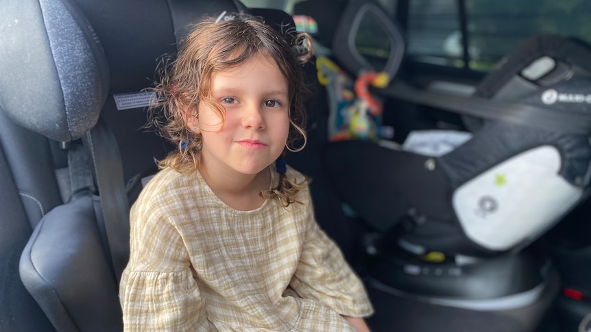 A young girl sits in a booster seat in the rear seat of a car.