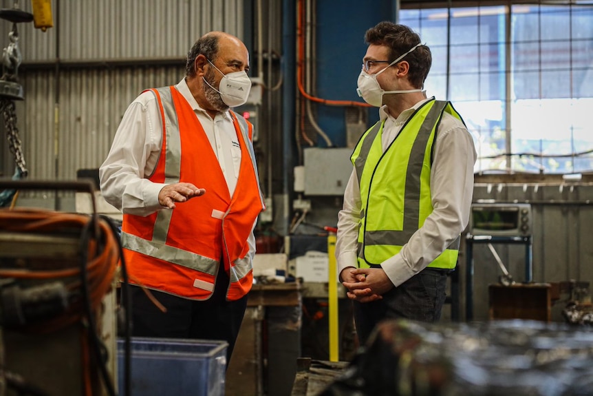 Two men in high vis vests stand talking to each other